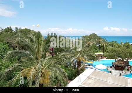 Una vista de un verde jardín, una piscina, un bar junto a la piscina y mar azul en el hotel de clase alta en el complejo mediterráneo en Turquía.