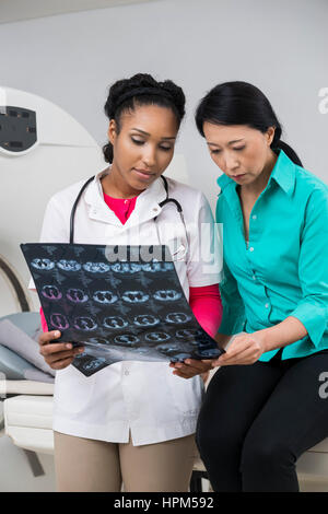 Doctora y seria mujer madura busca en tomografía computarizada de rayos x en la sala de examen de informe Foto de stock