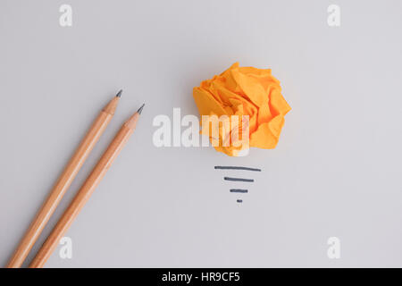 En busca de una nueva idea o innovación. Papel arrugado bola amarilla como una bombilla de luz y dos lápices.