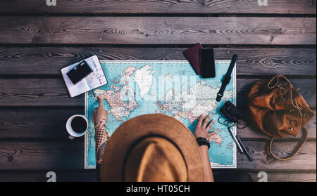 Señalización turística en Alaska en el mapa del mundo con sus accesorios de viaje alrededor. Mujer joven vistiendo sombrero marrón planeando una gira mirando el mundo ma