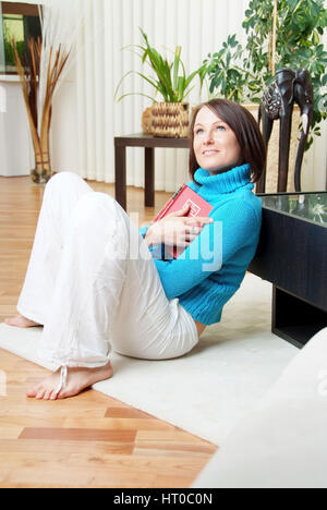 Junge Frau mit Buch am Wohnzimmerfu sitzt entspannt?Boden - joven con libro en casa Foto de stock