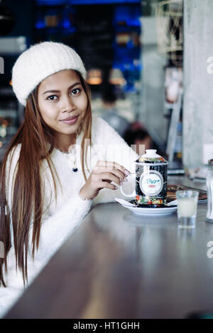 Hermosa muchacha con ropa blanca driniking té en un bar.