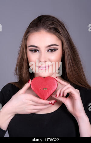 Mujer joven sosteniendo una caja de bombones con forma de corazón inscrito con la palabra amor. Foto de stock