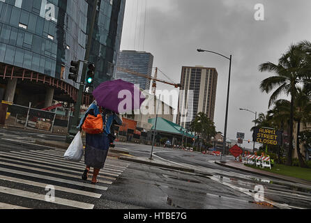 Honolulu, Hawaii, USA - Agosto 7, 2016: Una mujer no identificada con cruzar la calle paraguas en la lluvia bajo el cielo tormentoso en Honolulu, Oahu, Hawaii. Foto de stock