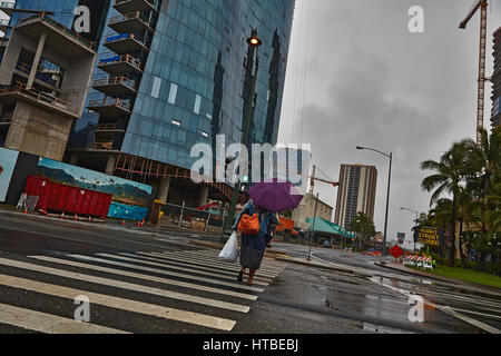 Honolulu, Hawaii, USA - Agosto 7, 2016: Una mujer no identificada con cruzar la calle paraguas en la lluvia bajo el cielo tormentoso en Honolulu, Oahu, Hawaii. Foto de stock