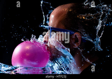 Retrato de un hombre con gafas de sol de goma de mascar y arrojaban agua en la cara contra un fondo negro Foto de stock