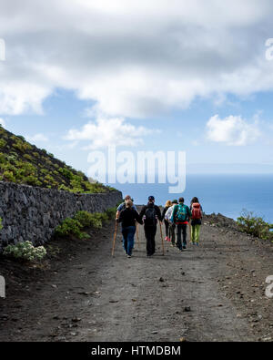 Hiking Trail, Fuencaliente. La Palma. Excursionistas turistas caminando por una carretera volcánica en su caminata guiada en la región de Fuencaliente de La Palma. La isla vecina La Gomera es visible en el horizonte, mirando al mar. Foto de stock