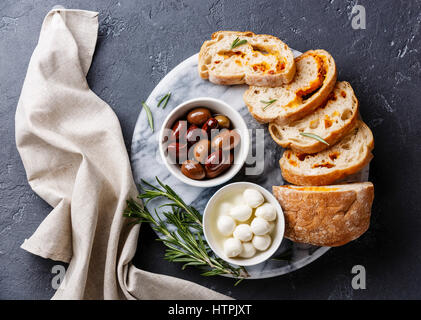 Aceitunas, mini queso Mozzarella y rodajas de pan ciabatta con queso sobre fondo oscuro