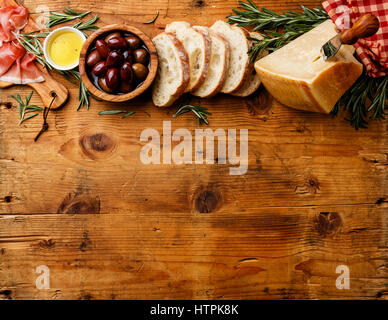 Comida italiana con jamón, rodajas de pan ciabatta, parmesano y aceitunas sobre fondo de madera espacio de copia