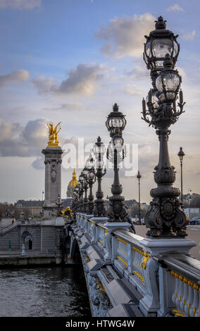 Luces a lo largo del puente Alexandre III puente sobre el río Sena en París, Francia. Vista mirando hacia el Musee de l'Armee adornada con estatuas de oro.