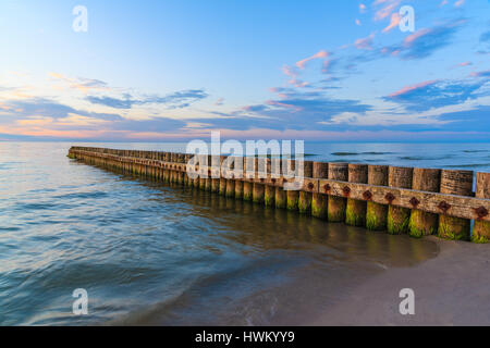 Puesta de sol sobre el mar con espigones de madera en primer plano en Leba playa, Mar Báltico, Polonia