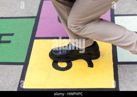 Chico jugaba me un colorido juego de la rayuela pintada en el pavimento Foto de stock