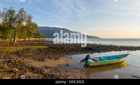 Una pequeña embarcación de madera verde y azul atada sobre ABC Beach en la isla de Tioman, Malasia, como los atardeceres y sube la marea. Foto de stock