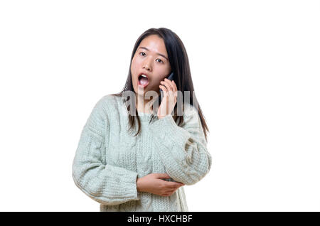 Atractiva joven China reaccionar en estado de shock y consternación de pie con la boca abierta en la noticia que acaba de escuchar en su teléfono móvil, aislado en w Foto de stock