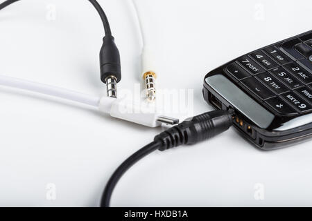 Accesorios de telefonía celular móvil, enchufe los auriculares, conectores aislados en un fondo blanco con un negro teléfono con teclado Foto de stock