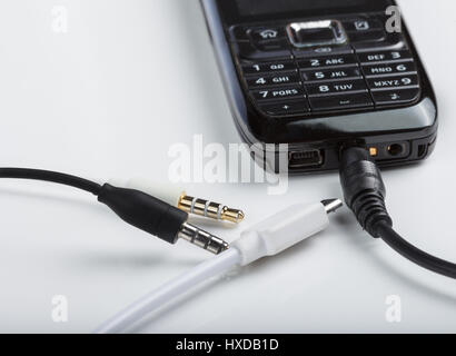 Accesorios de telefonía celular móvil, enchufe los auriculares, conectores aislados en un fondo blanco con un negro teléfono con teclado Foto de stock