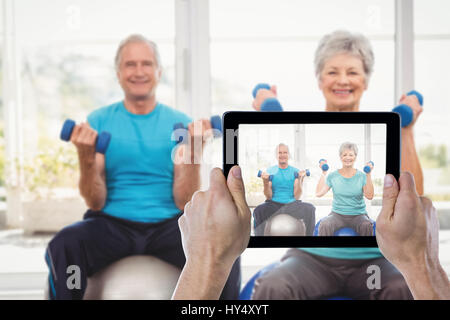 Mano sujetando recortadas contra la tableta digital retrato de pareja senior sonriente sosteniendo pesas