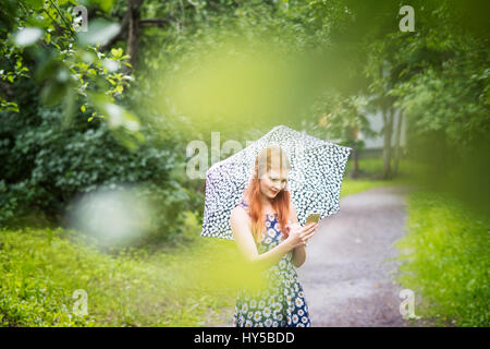 Finlandia, Pirkanmaa, Tampere, mujer vistiendo vestido floral con sombrilla permanente en el parque