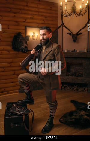 Hombre cazador respetable en ropa de caza con estilo vintage con rifle  antiguo contra chimenea.