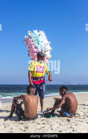 Brasil, Rio de Janeiro: El hombre que vende algodón dulce con amigos en la playa de Copacabana Foto de stock