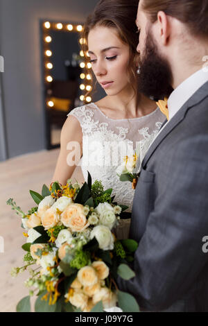 Retrato de una hermosa novia con un ramo y el novio con una barba en la habitación del hotel Foto de stock