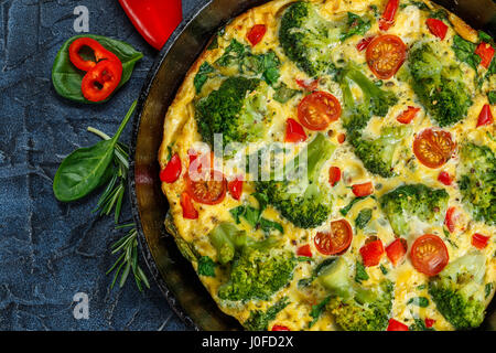 Frittata con el brócoli, la espinaca, pimientos y tomates en la sartén de hierro. Clase de italiano tortilla con verduras.