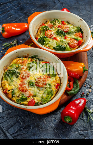 Frittata con el brócoli, la espinaca, pimientos y tomates en dos formas de cerámica para hornear. El italiano tortilla con verduras.