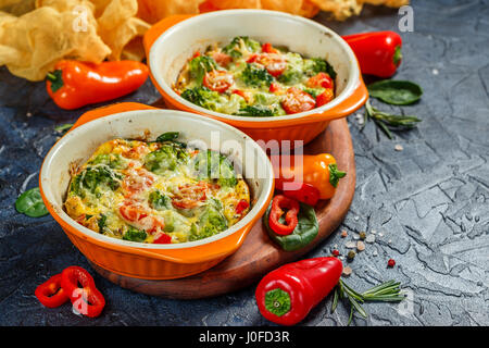 Frittata con el brócoli, la espinaca, pimientos y tomates en dos formas de cerámica para hornear. El italiano tortilla con verduras.