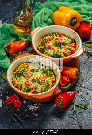Frittata con el brócoli, la espinaca, pimientos y tomates en dos formas de cerámica para hornear. El italiano tortilla con verduras.