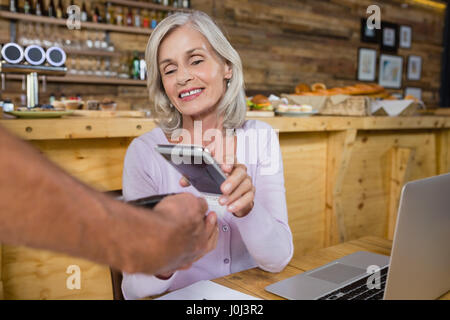Senior mujer haciendo el pago mediante tecnología NFC en teléfonos móviles en cafÃƒÂ© Foto de stock