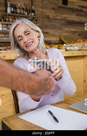 Senior mujer haciendo el pago mediante tecnología NFC en teléfonos móviles en cafÃƒÂ© Foto de stock