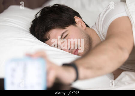 Sleepy man apagar el despertador, hora de despertar Foto de stock