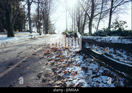Una ligera cubierta de nieve sobre caído hojas de otoño y a lo largo de una valla y la ruta. Foto de stock