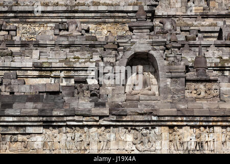 Una estatua de Buda meditando rodeada por relieves en piedra en el Borobudur en Indonesia, en Asia.