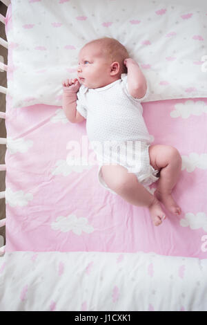 Niña de dos semanas durmiendo en su cuna en hojas rosadas con patrón nuboso.