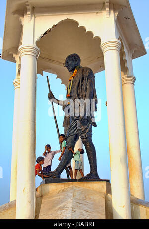 Estatua de Mahatma Gandhi en el paseo marítimo de Pondicherry, India, con niños jugando. Foto de stock