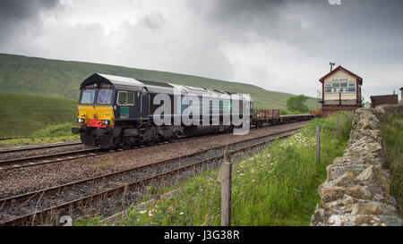 Una clase de 66 locomotoras de ferrocarril diesel pesados de mercancías tirando de un tren que cruza Blear Moor Settle-Castle cumbre sobre la línea de ferrocarril.