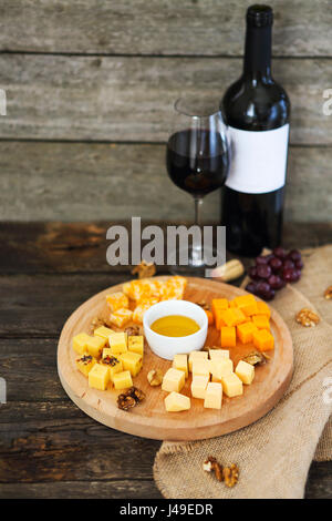 Uva, conjunto de diferentes tipos de quesos con un vaso de vino tinto en la mesa de madera