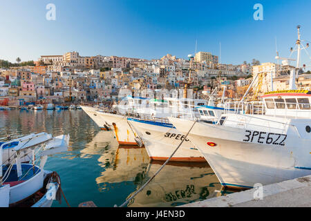 Barcos pesqueros amarrados en el puerto rodeado por el azul del mar y el casco antiguo de la ciudad, Sciacca, provincia de Agrigento, Sicilia, Italia Foto de stock