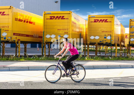 Mujer ciclista que pasa alrededor de contenedores de transporte de DHL. Dobroviz, República Checa, Europa