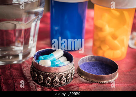Vintage metálico pastillero abierto con pastillas de color blanco a lo largo de un vidrio de agua Foto de stock