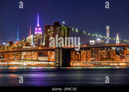 Vista nocturna del Puente de Brooklyn y Manhattan rascacielos con el edificio Empire State iluminado en color rosa. La Ciudad de Nueva York