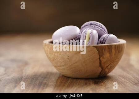 Violeta macarons en madera tazón en mesa de madera Foto de stock
