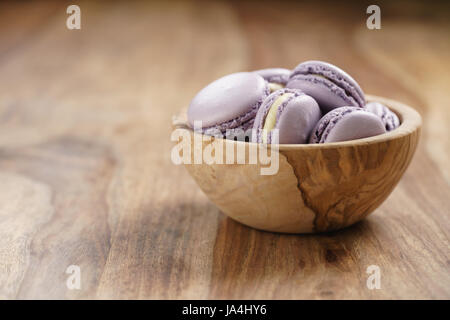 Violeta macarons en madera tazón en mesa de madera Foto de stock