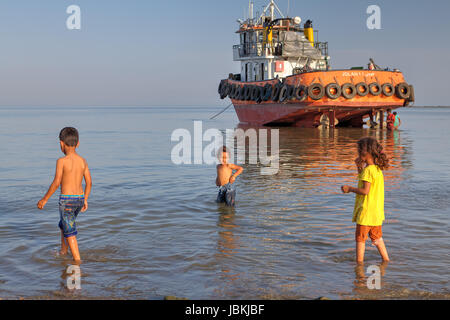 Tres niños desnudos jugando en el mar Arábigo en la playa Mahim en