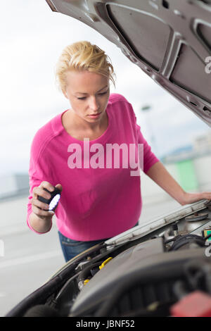 Auto-suficientes seguros muchacha moderna inspeccionando el motor del coche roto con una linterna en la mano. Foto de stock