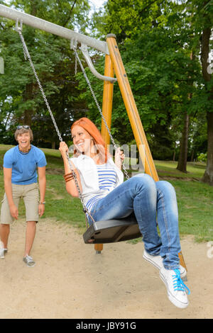 La pareja de adolescentes juguetona chica sentada en el columpio en el parque Foto de stock