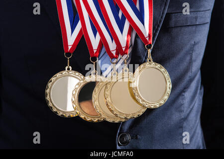 Parte media del empresario luciendo medallas de oro contra el fondo negro Foto de stock