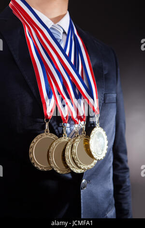 Parte media del empresario luciendo medallas de oro contra el fondo negro Foto de stock