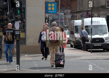 Hombre de negocios turista con maletas trolley maletín con ruedas en las calles de Glasgow Crossing Road hasta el destino o el hotel Foto de stock